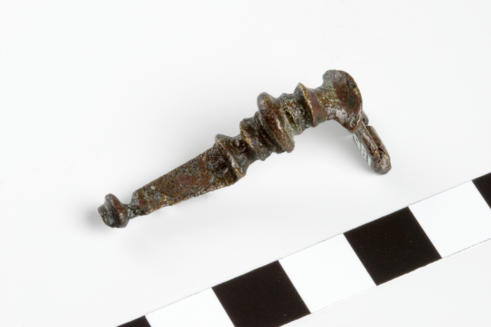 Bronze 'T'-shaped brooch with five cross ribs on the upper bow, a flat tapering ...